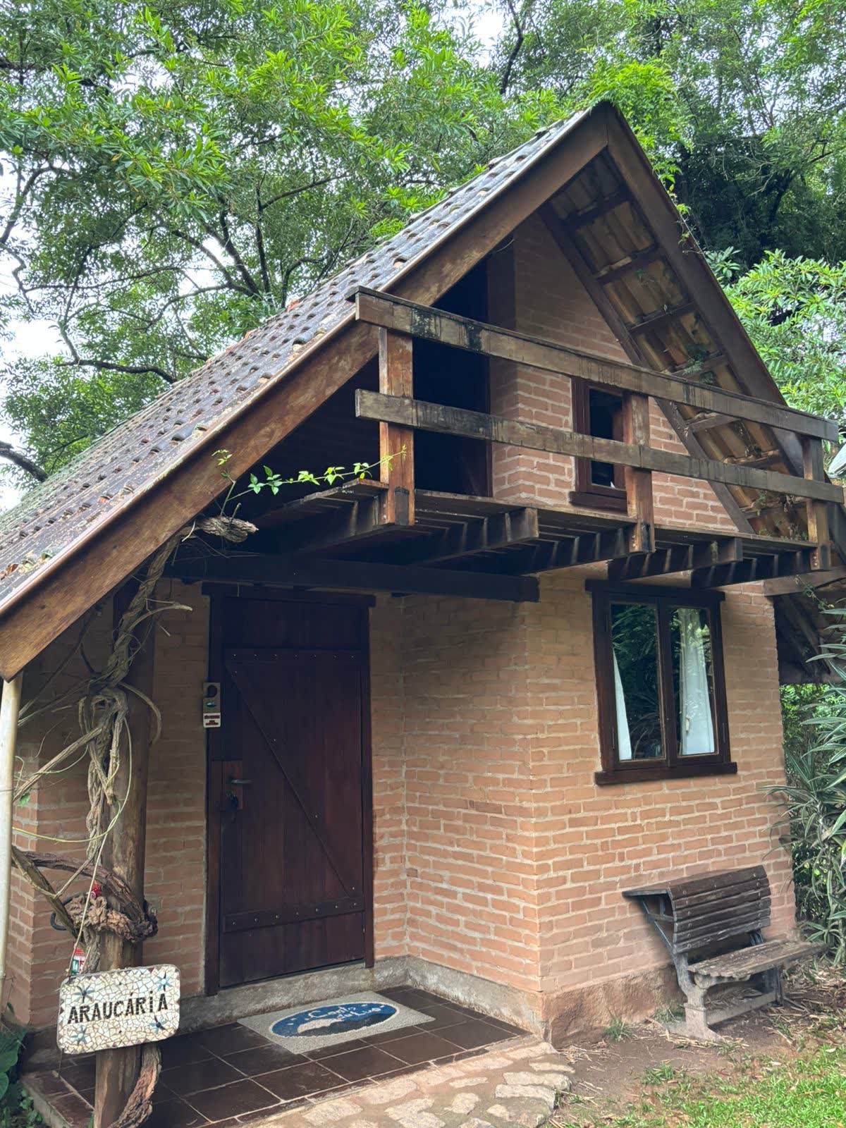 Entrada do chalé, com a placa Araucária e o banco de madeira