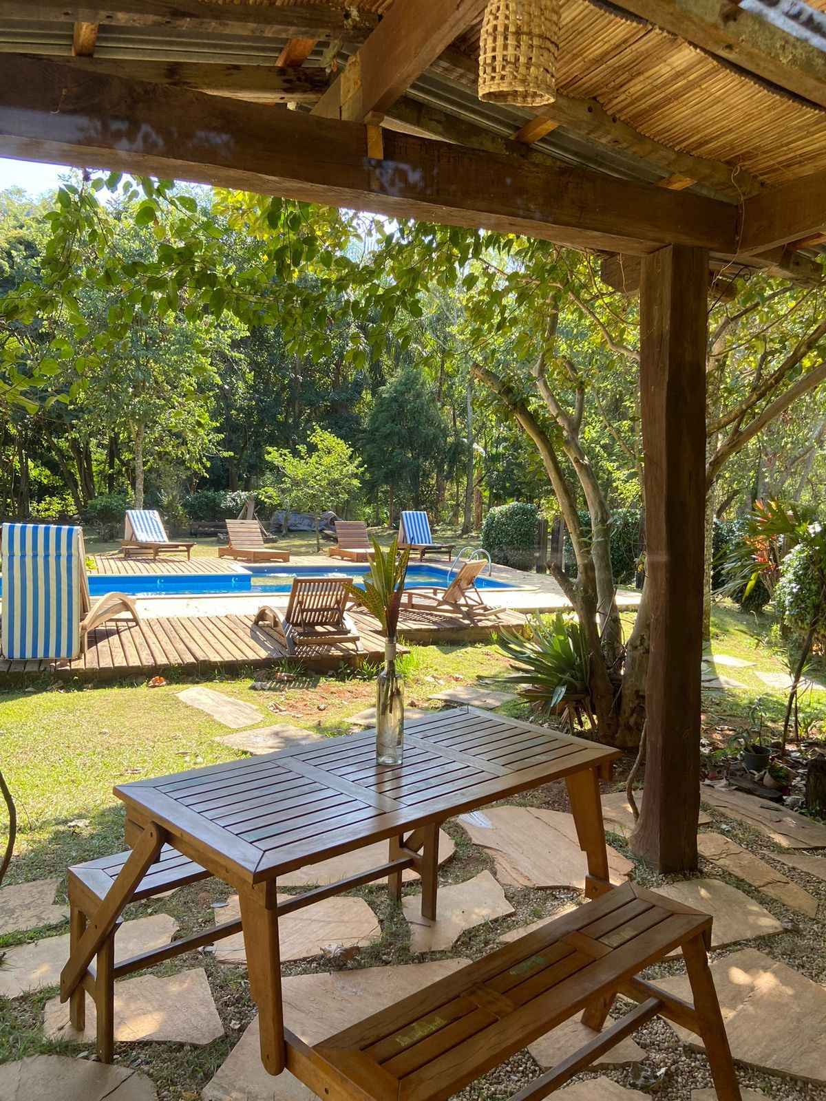 Mesa de madeira sob o pergolado, de frente para a piscina e o jardim