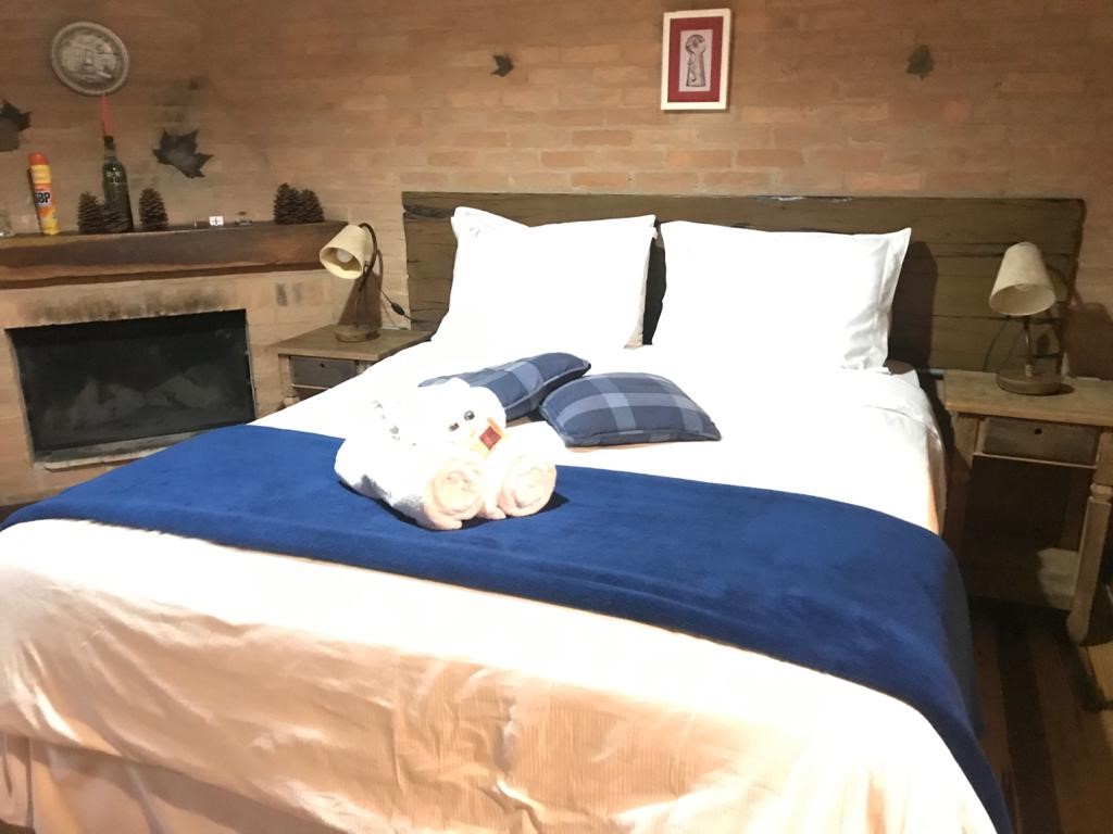 Cama do Chalé Eucalipto com manta azul, toalhas e almofadas xadrez, lareira ao lado