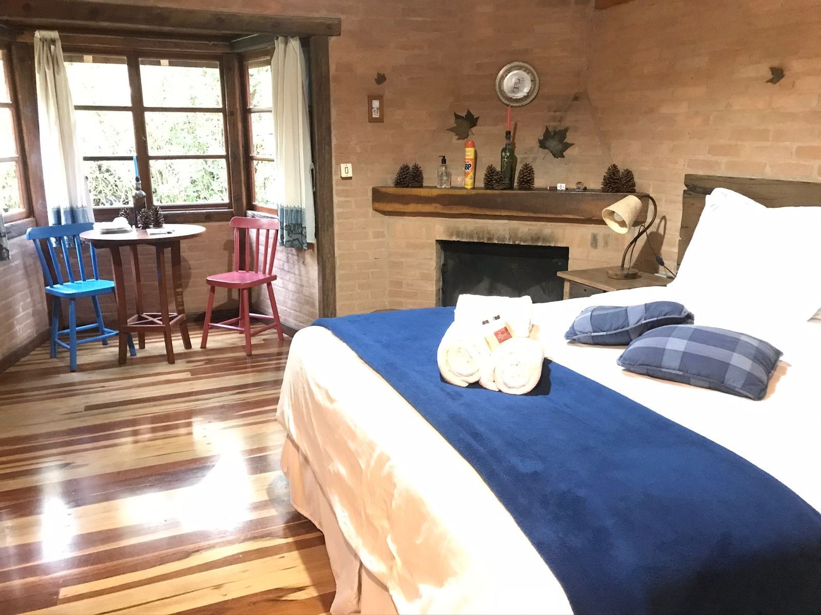 Cama com manta azul e toalhas dobradas, lareira e mesa ao fundo