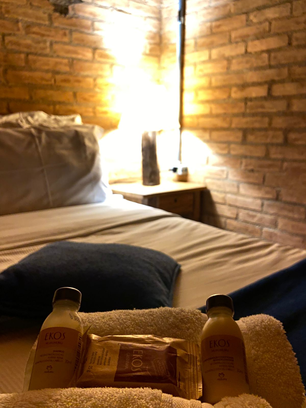Amenities sobre as toalhas, com a cama e o abajur ao fundo