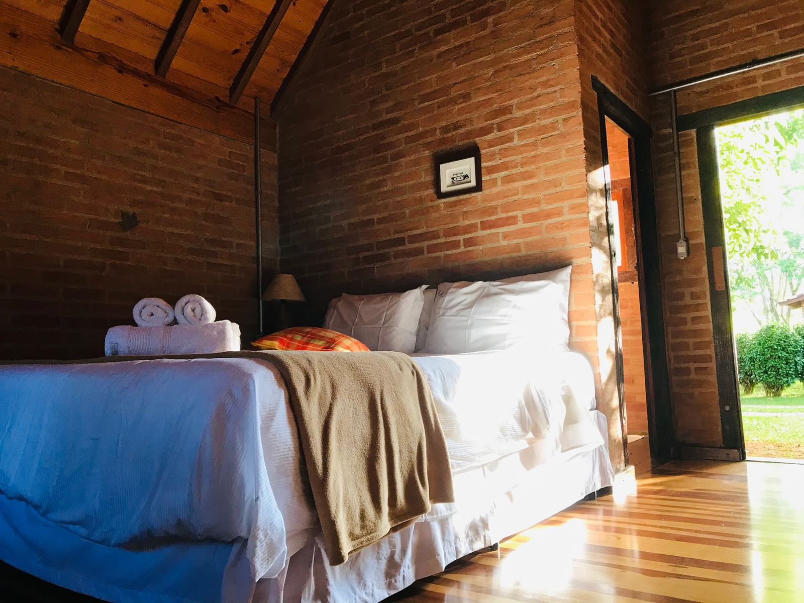 Cama com manta bege e a porta aberta para o jardim