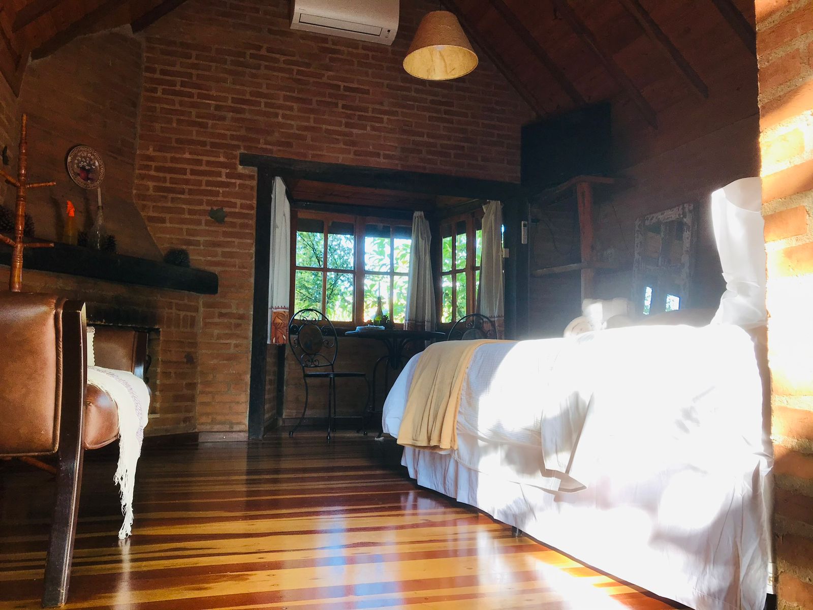 Cama iluminada pela janela, sofá e lareira do Manacá