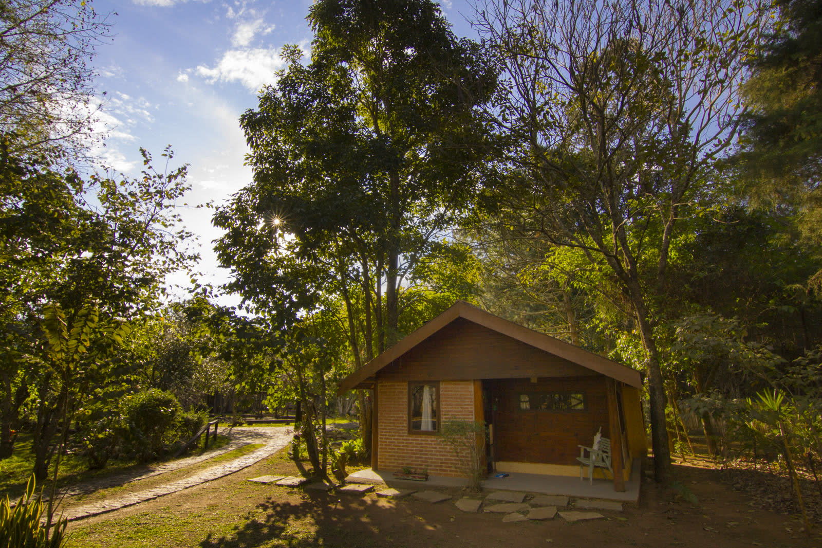 Chalé Paineiras: fachada com o sol entre as árvores