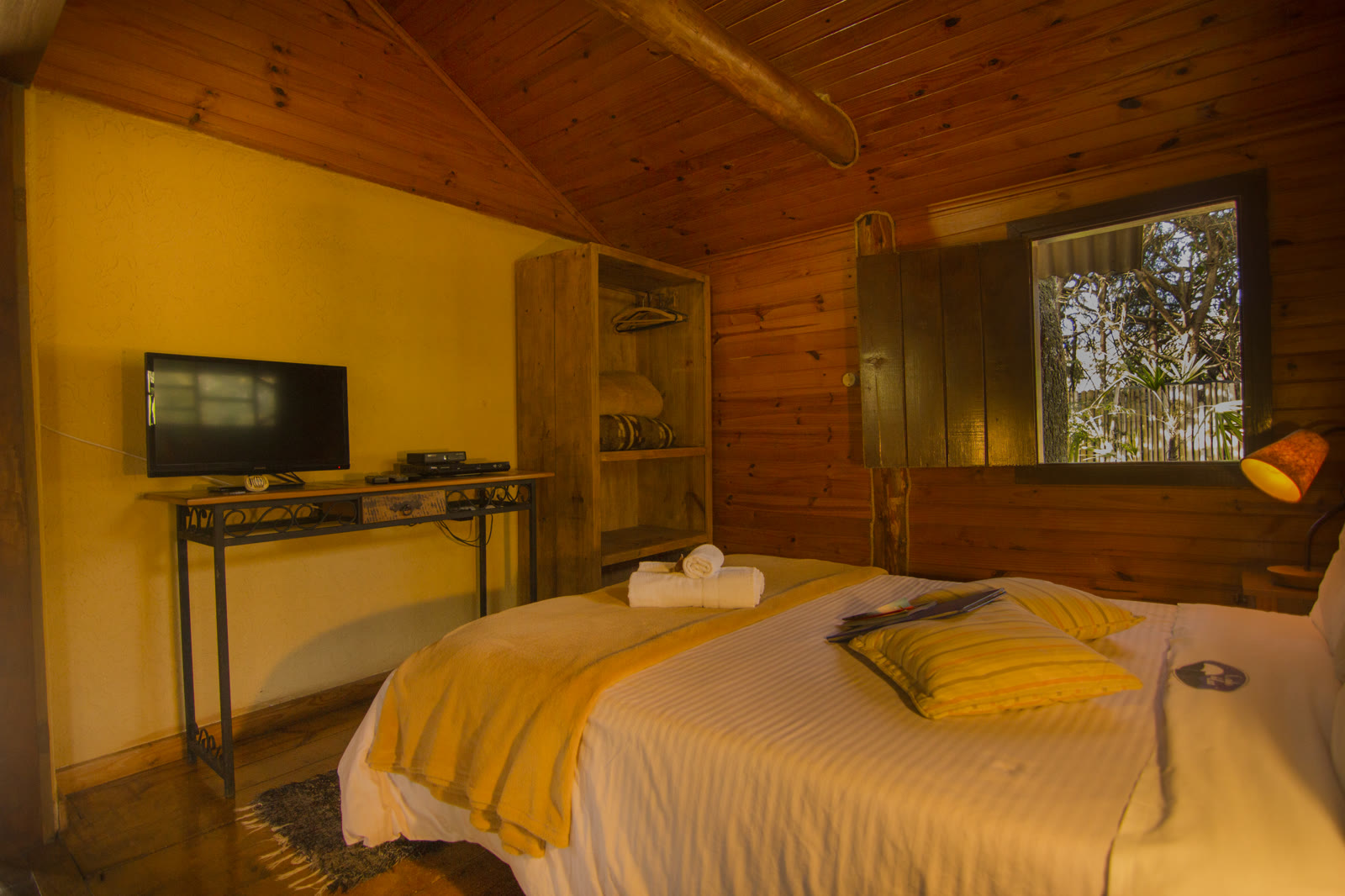Quarto do Paineiras com TV, armário aberto e cama com manta amarela