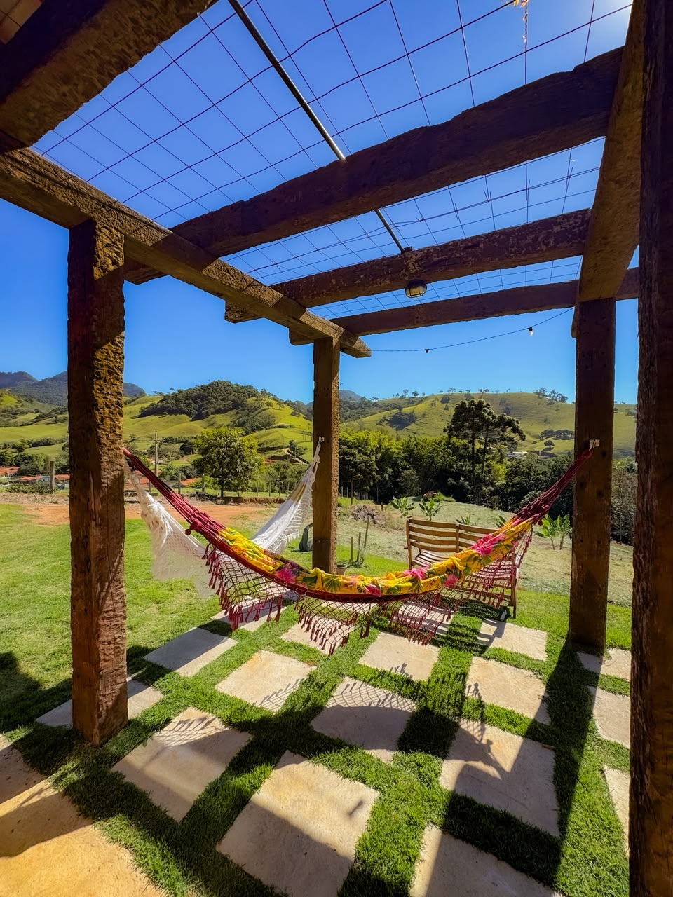 Redário da Morada Canto do Sol, com as redes sob o pergolado e os morros ao fundo